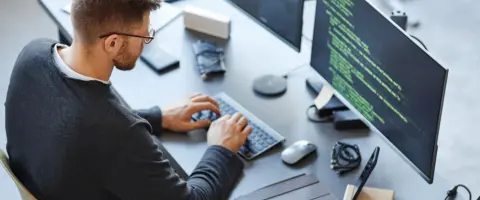 Ein Mitarbeiter aus der Telekommunikation & Softwaretechnik sitzt vor seinem Computer und programmiert.
