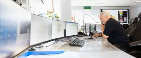 Ein Mann sitzt an einem Arbeitsplatz mit vielen Bildschirmen.