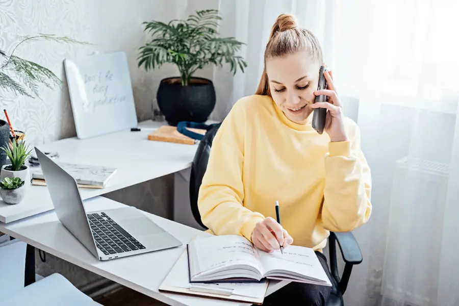 Mitarbeiterin telefoniert am Arbeitsplatz und macht sich Notizen.
